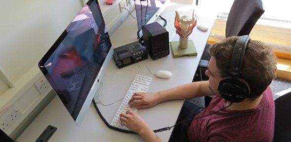 Participant in linguistic research sitting at computer and wearing headphones